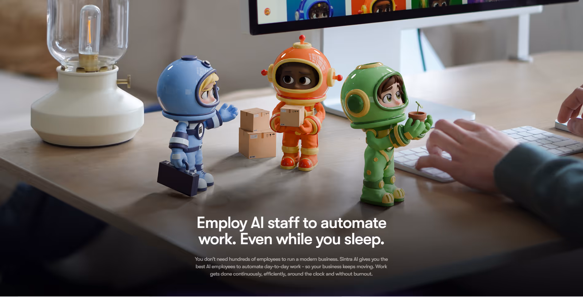 Three small cartoon characters in blue, orange, and green suits on a desk near a keyboard and lamp.