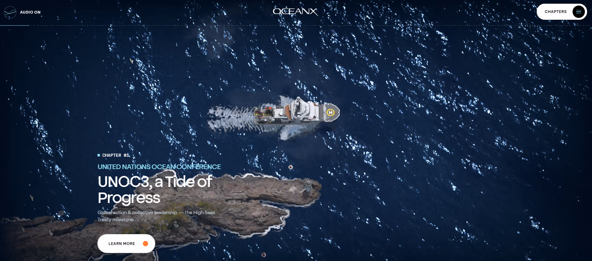 Aerial view of a ship sailing near rocky coastline in deep blue ocean water with sunlight reflections.